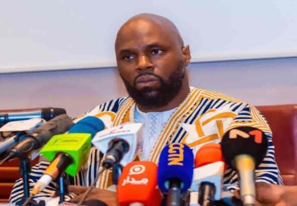 Kemi Séba lors d'une conférence à Pretoria, entouré de microphones de médias.